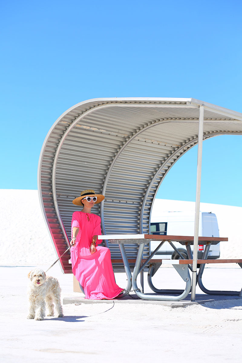 woman wearing hat, pink caftans, and sunglasses and sitting with her dog 