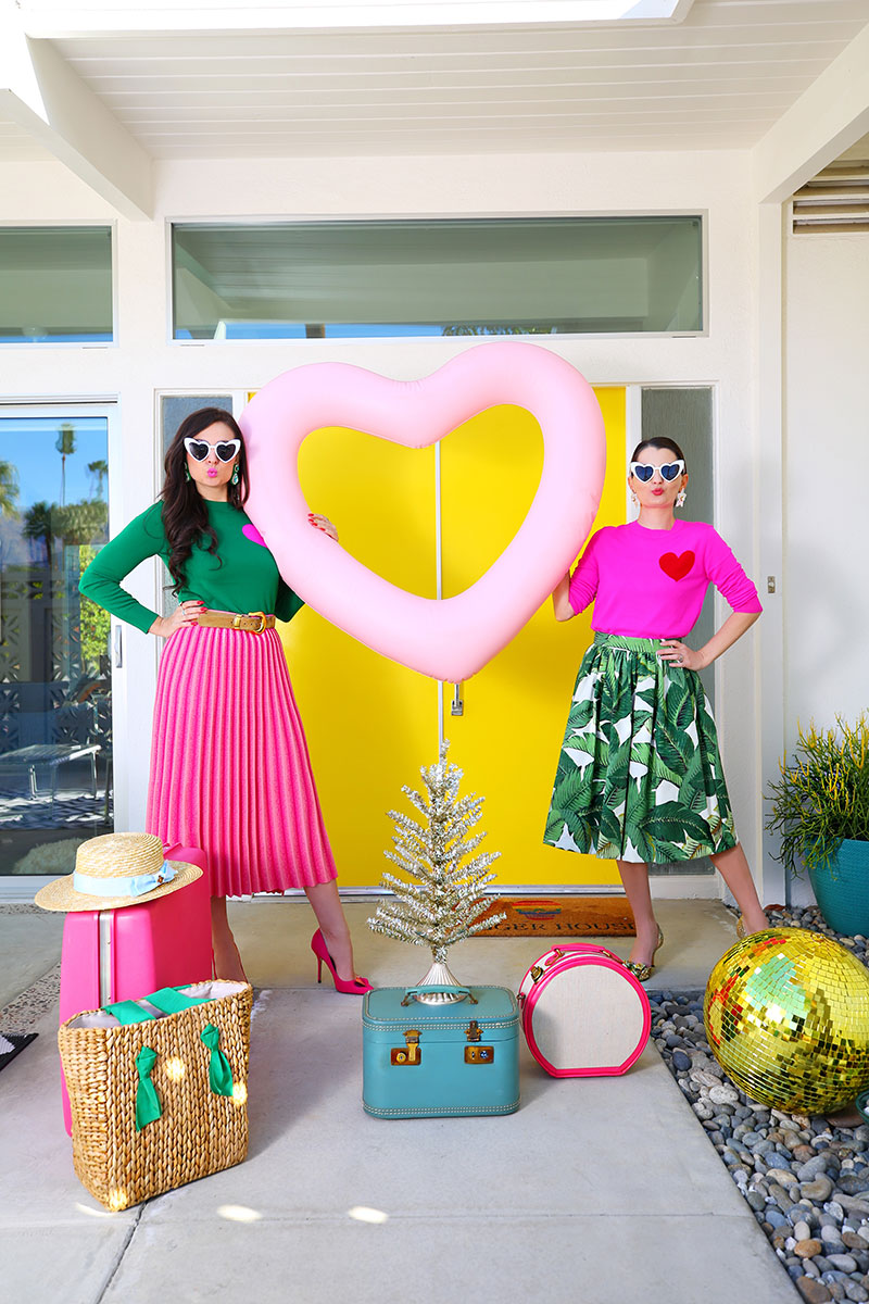two women holding pink heart shaped balloon and are surrounded by bags