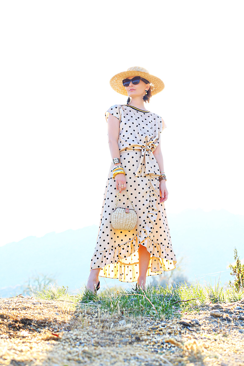 woman wearing hat, sun glasses, polka dot dress, and holding a hand bag