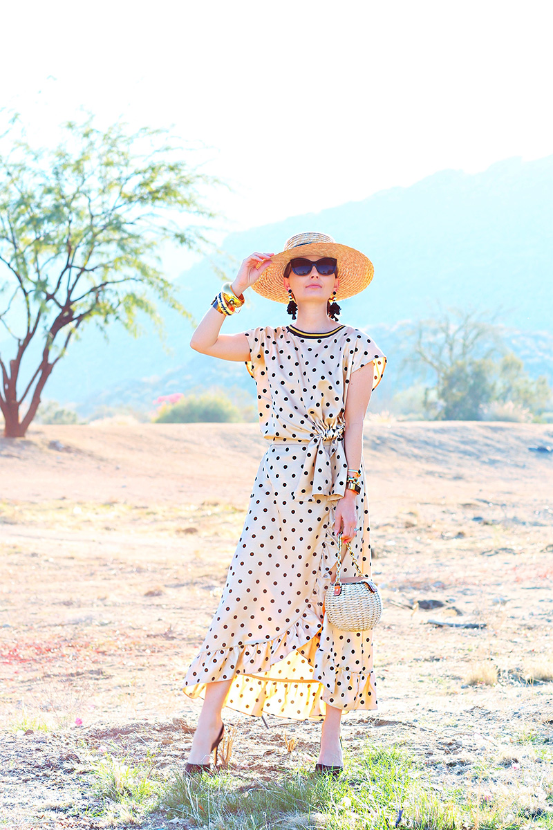 woman standing in the outdoors holder her hat and wearing a polka dot dress