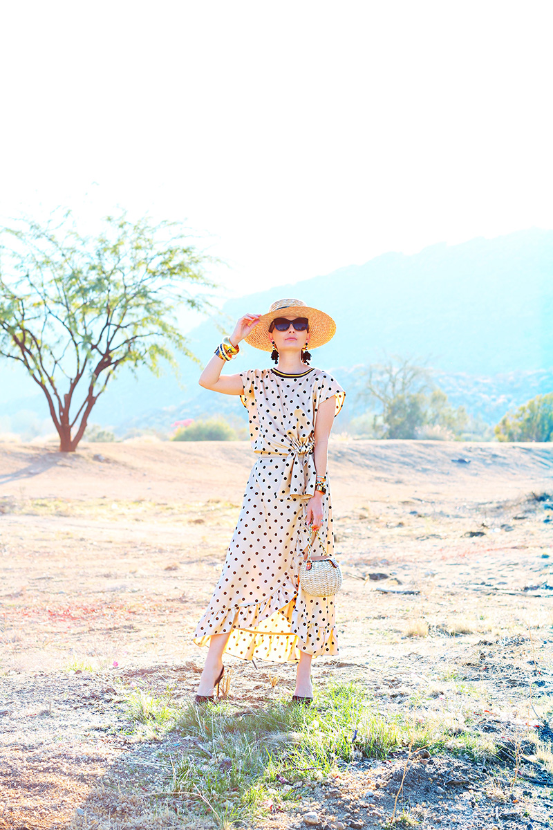 woman standing in the outdoors wearing a dress, hat, and sunglasses