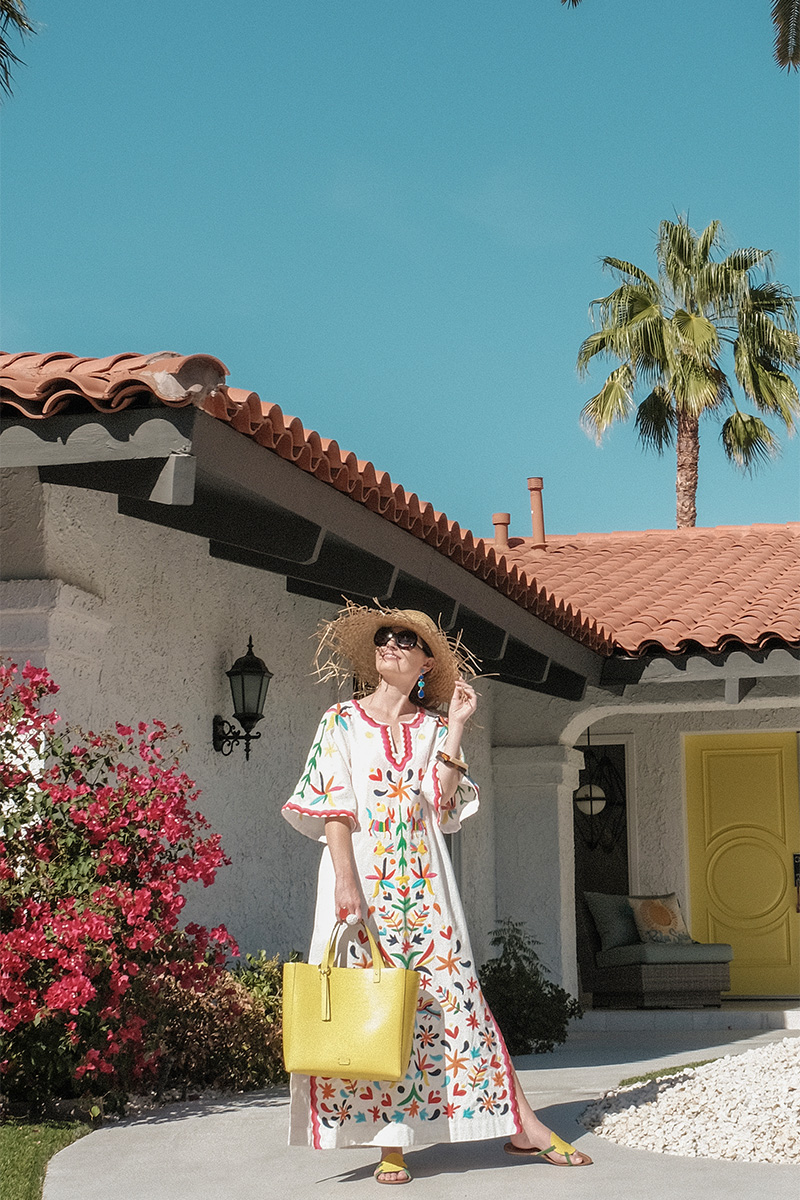 woman wearing FRANCES VALENTINE PALM SPRINGS caftan, weaved hat, and yellow bag for where to find caftans