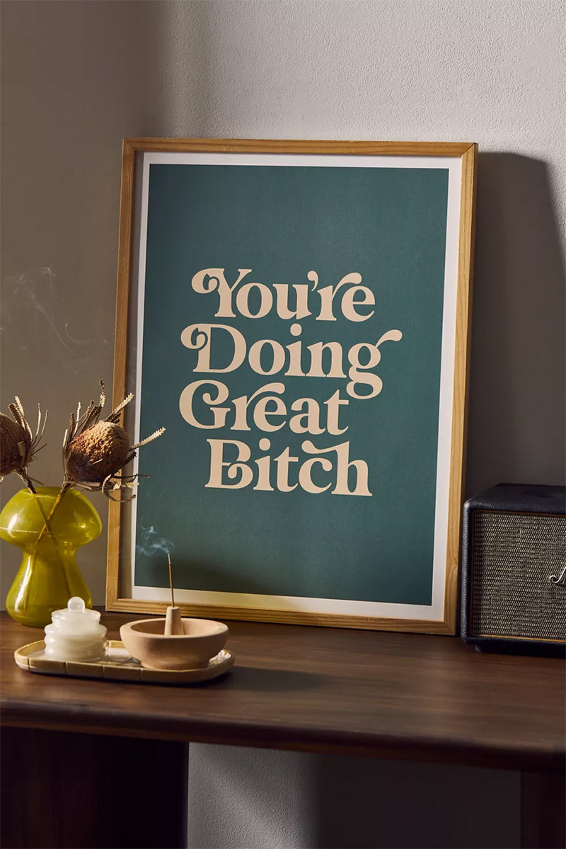 Art print that reads You're Doing Great Bitch in fancy font on green colored background, in a natural wood frame.