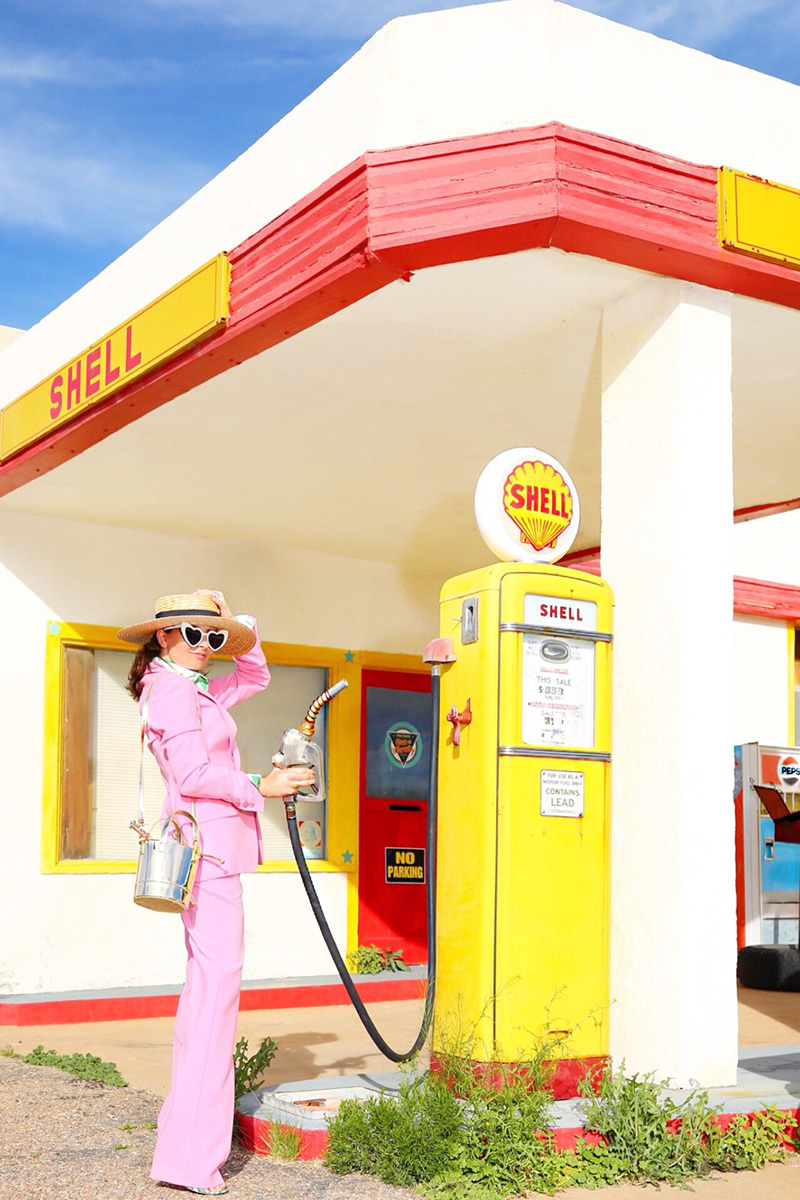 A brunette wears a pink pantsuit while pumping gas at a vintage gas station in Bisbee, Arizona.