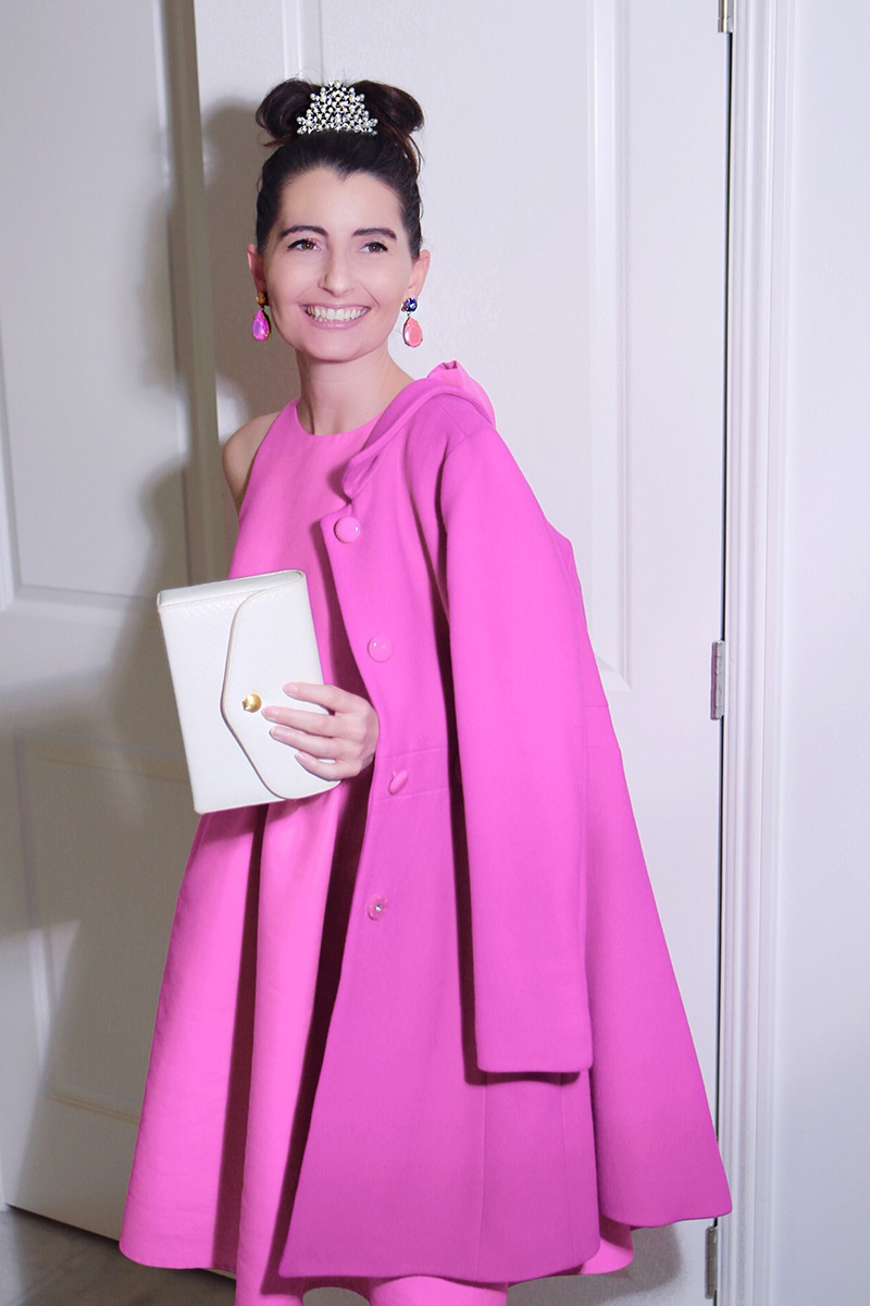 A brunette wears a knee-length pink coat and dress in the style of Audrey Hepburn at Breakfast at Tiffany's.