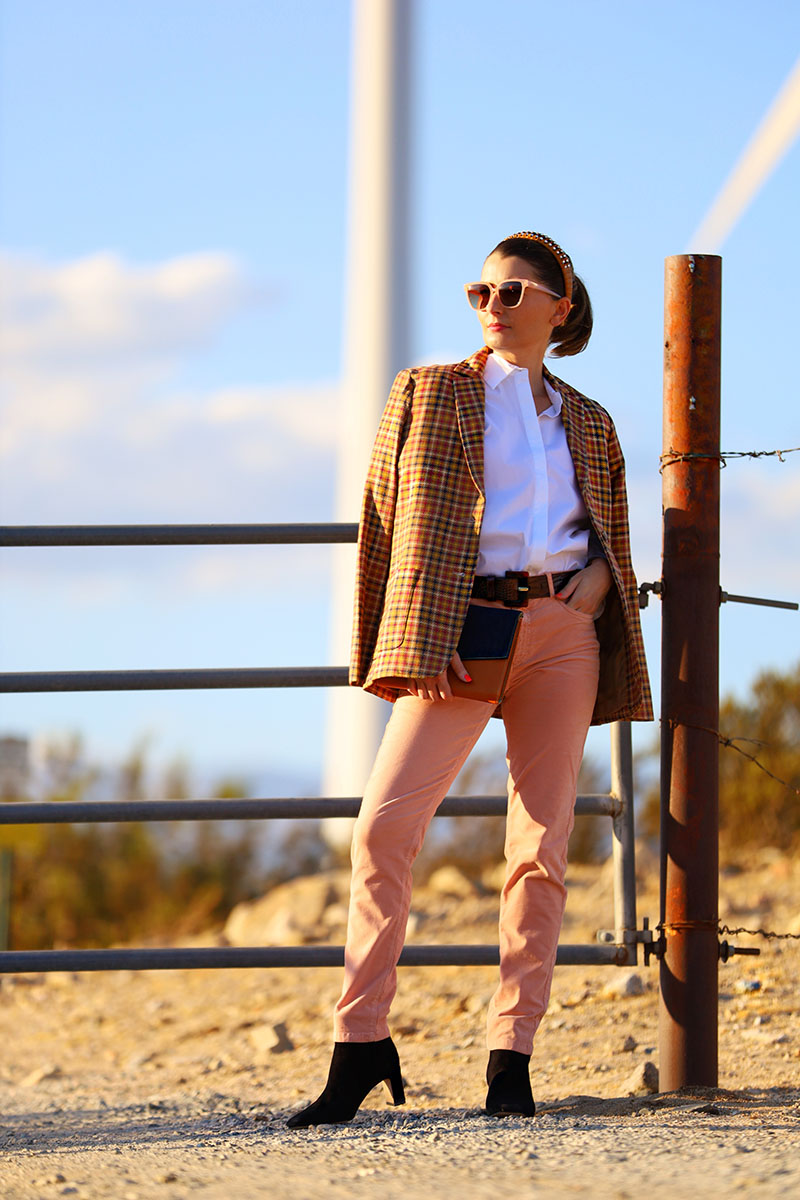 Fashion blogger Kelly Golightly wears a houndstooth blazer with pink velvet pants and a white button-down shirt. She holds a denim clutch and wears black suede boots.