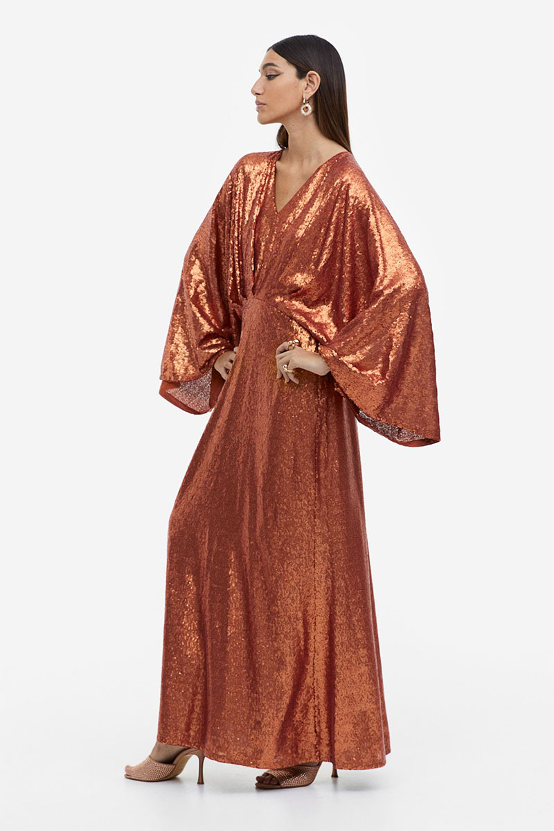 A brunette woman wears an affordable caftan made of bronze sequins.